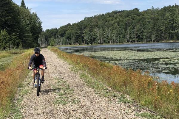 A cyclist pedals on the causeway over Lake Colby located on the Adirondack Rail Trail