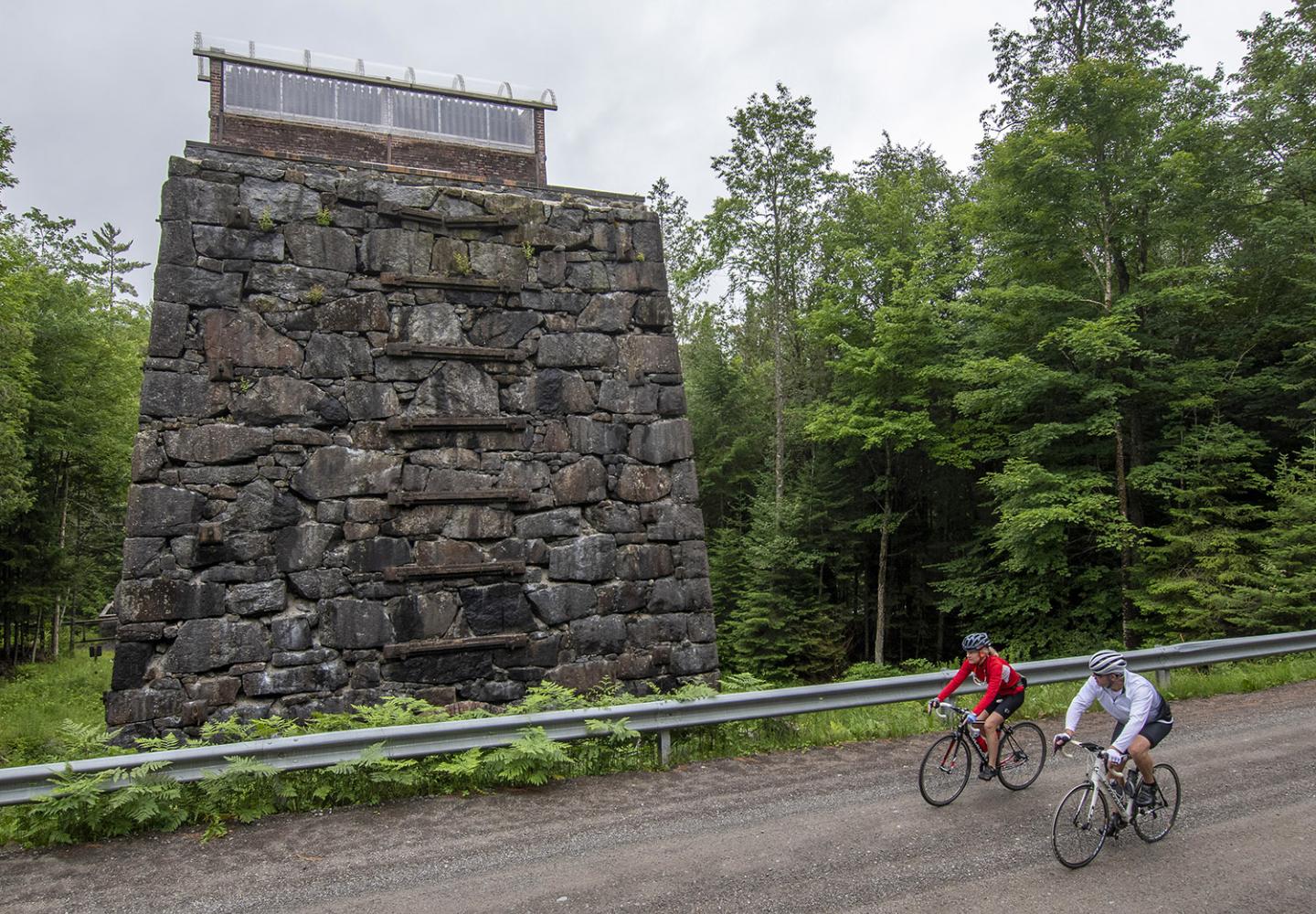 Cyclist pedal past the McIntire Furnace located on Open Space Institute property in Tahawus.