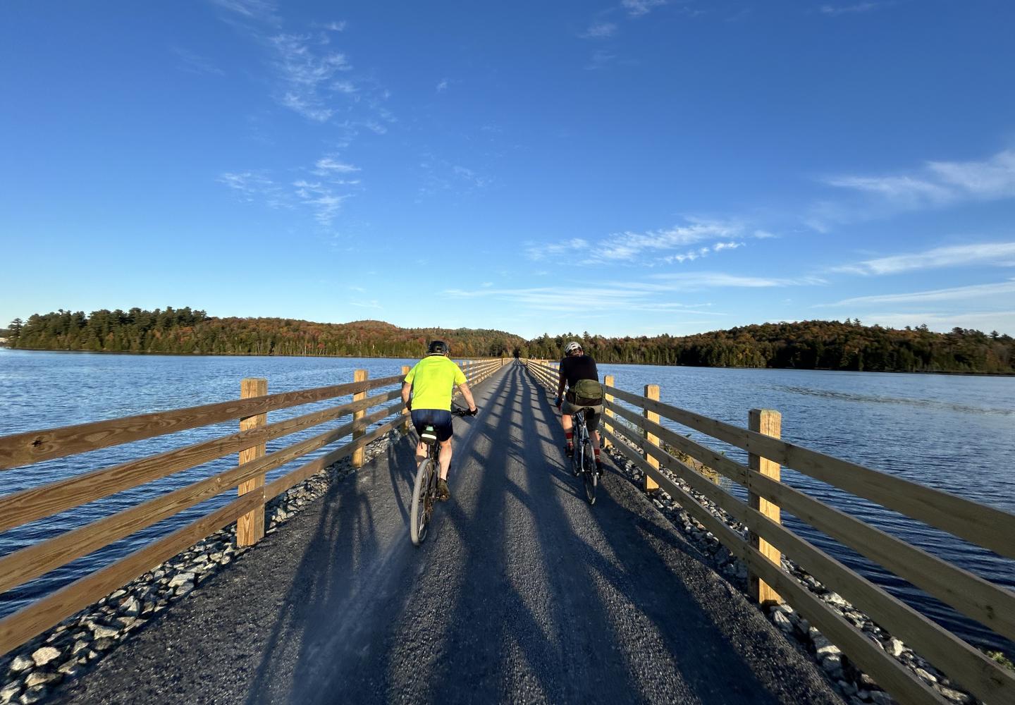 Cyclist ride across the Lake Colby causeway on the Adirondack Rail Trail outside of Saranac Lake.