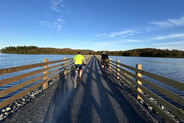Cyclist ride across the Lake Colby causeway on the Adirondack Rail Trail outside of Saranac Lake.